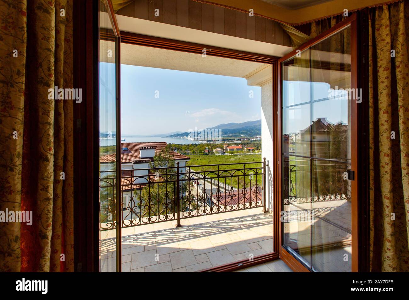 The open door on to the verandah of a luxury cabin with a view of the mountains and the sea. Glass door with wooden frame, dark curtains. Novorossiysk Stock Photo