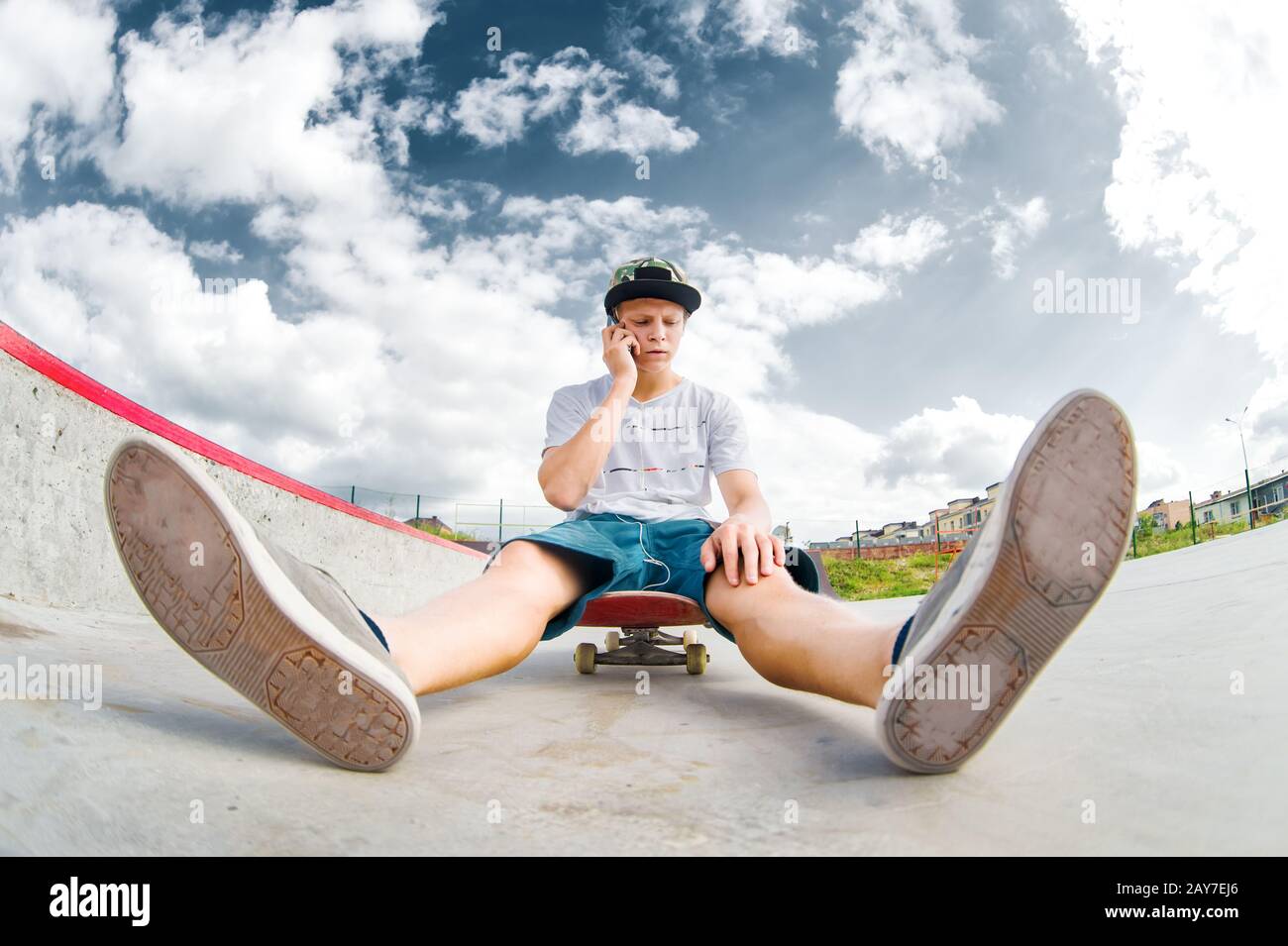 Young skater sitting on skateboard in park and talking on phone Stock Photo