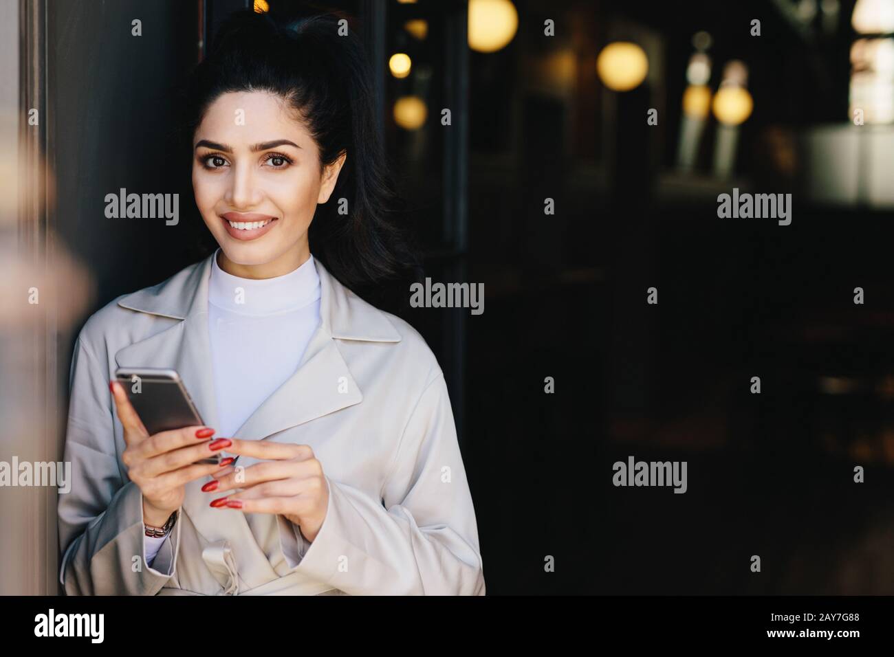 Attractive brunette businesswoman having dark hair tied in pony tail and wonderful make-up smiling demonstrating her white perfect teeth waitng for he Stock Photo