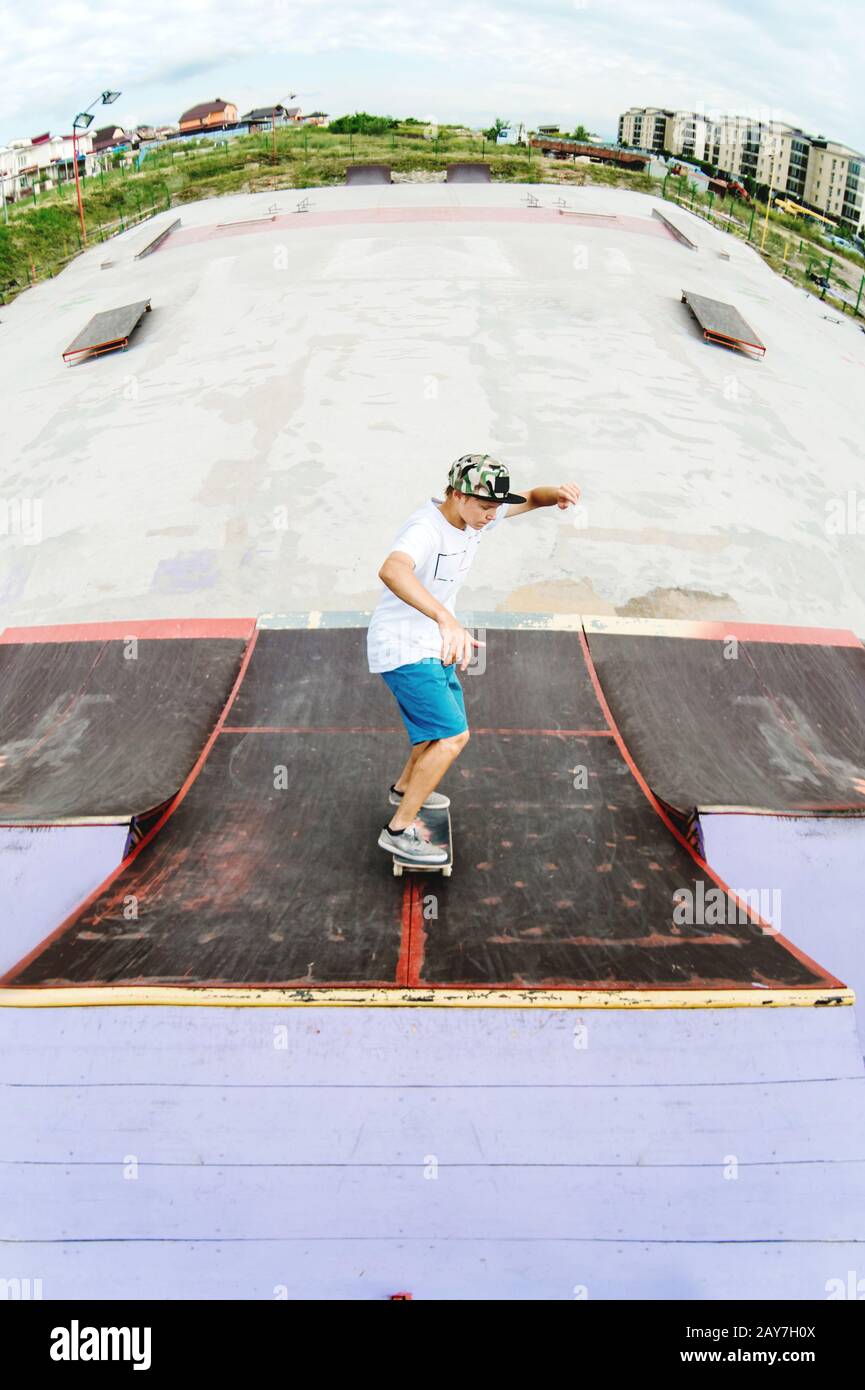 Teen skater rides over a ramp on a skateboard in a skate park Stock Photo