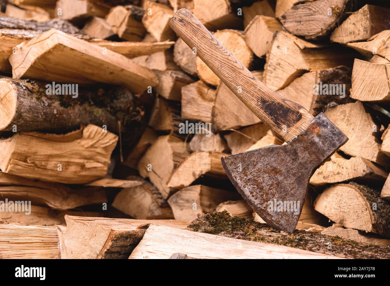 The ax is stuck in a log against the backdrop of chopped firewood lying in a flat pile Stock Photo