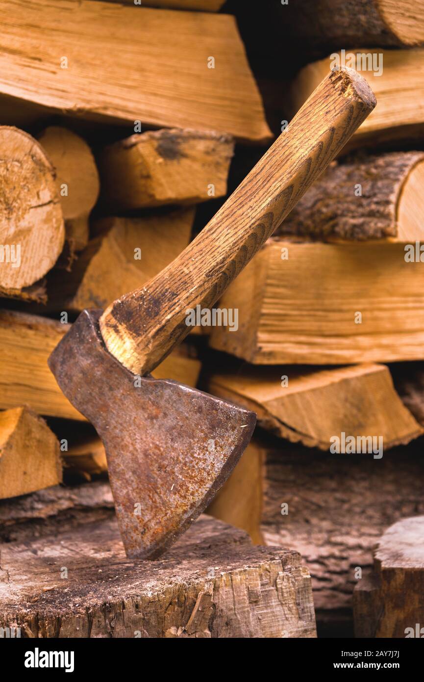 The ax is stuck in a log against the backdrop of chopped firewood lying in a flat pile Stock Photo