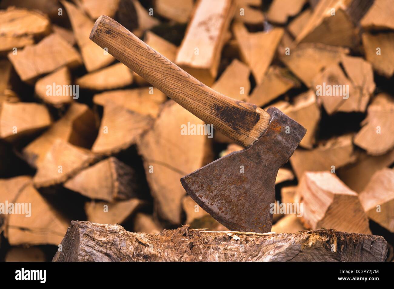 The ax is stuck in a log against the backdrop of chopped firewood lying in a flat pile Stock Photo