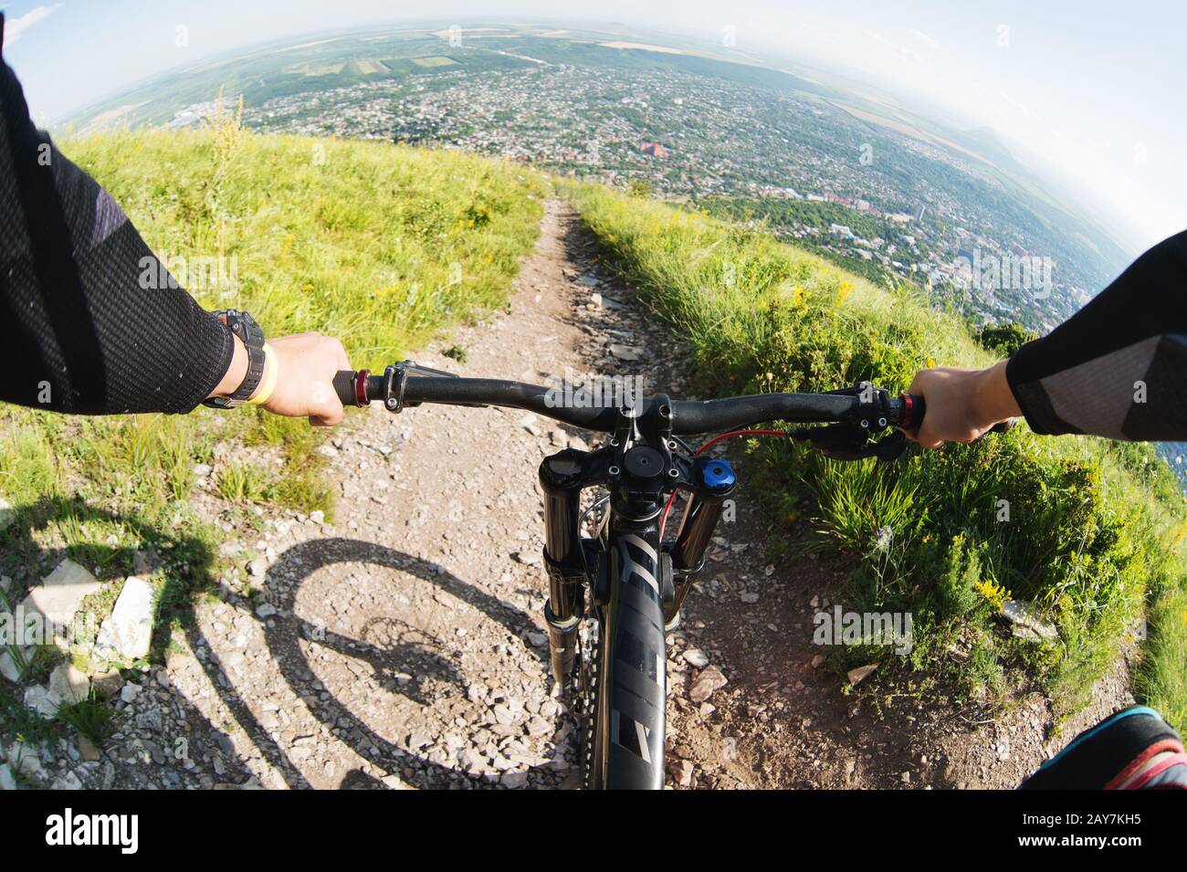 View from the first person of a cyclist riding downhill from a high mountain in the background of a city in the distance Stock Photo