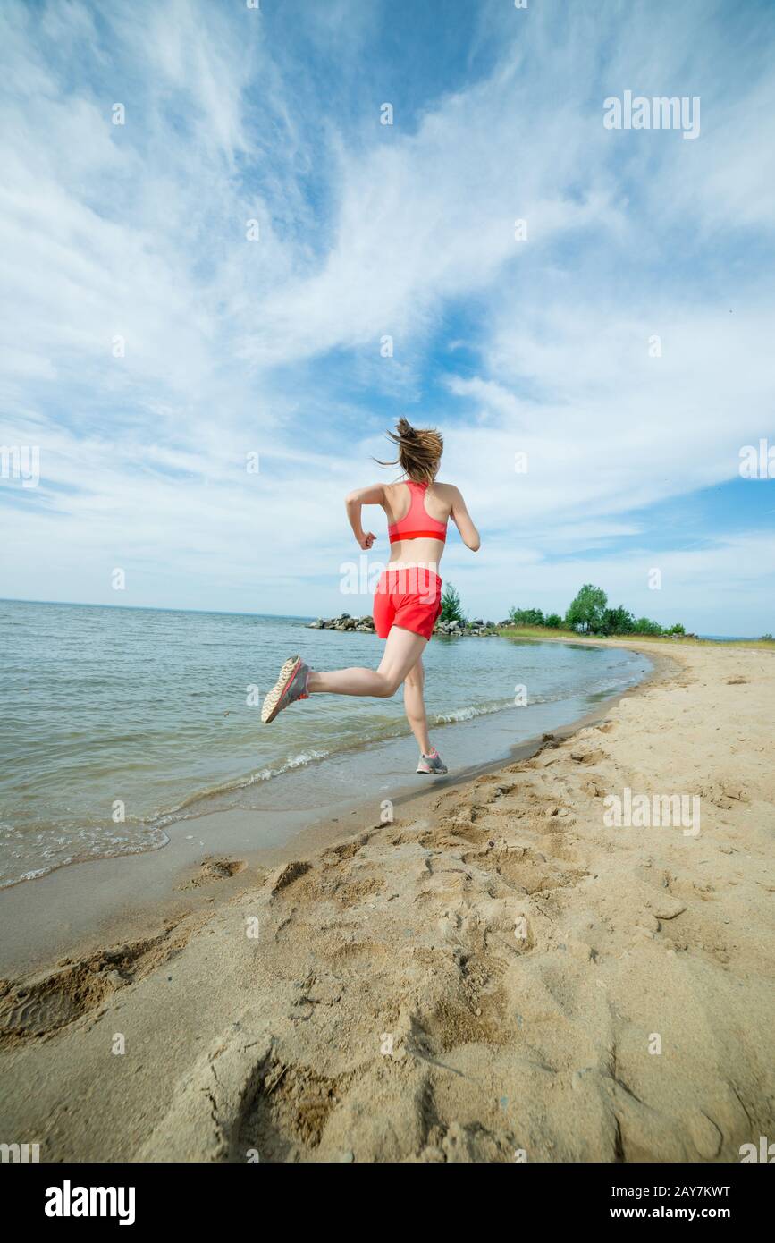 Young lady running at the sunny summer sand beach. Workout.  Jog Stock Photo