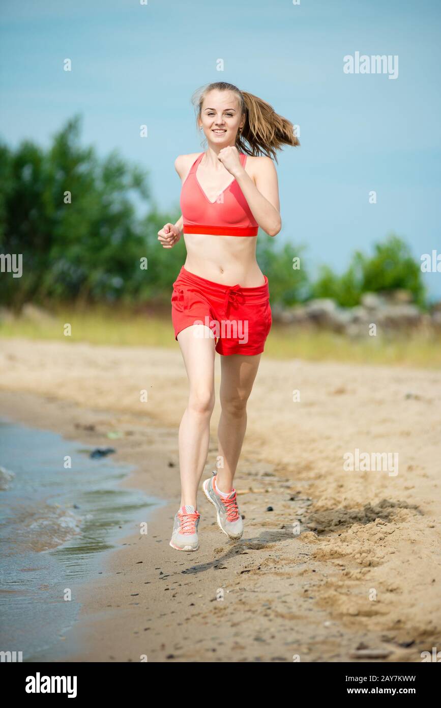 Young lady running at the sunny summer sand beach. Workout.  Jog Stock Photo