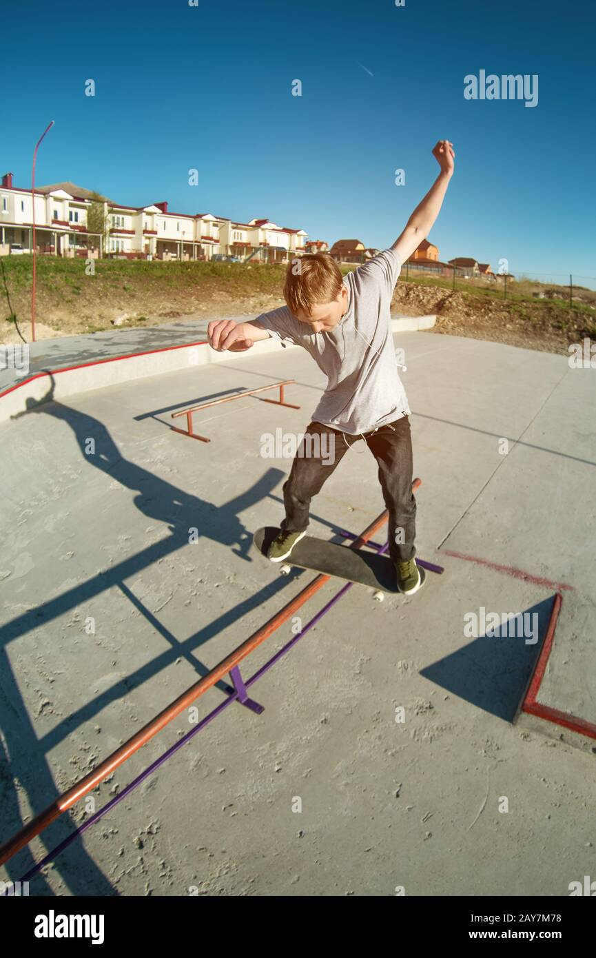 Teen skater in a hoodie sweatshirt and jeans slides over a railing on a skateboard in a skate park Stock Photo