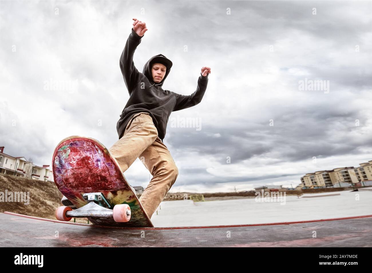 Teen skater in a hoodie sweatshirt and jeans slides over a railing on a skateboard in a skate park Stock Photo