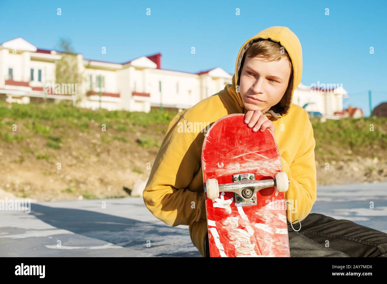 Close-up of a teenager dressed in a jeans hoodie sitting in a skate park and holding a skateboard Stock Photo