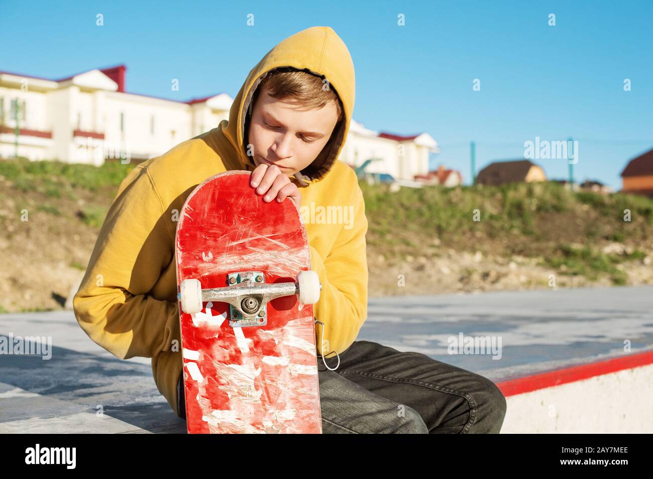 Close-up of a teenager dressed in a jeans hoodie sitting in a skate park and holding a skateboard Stock Photo