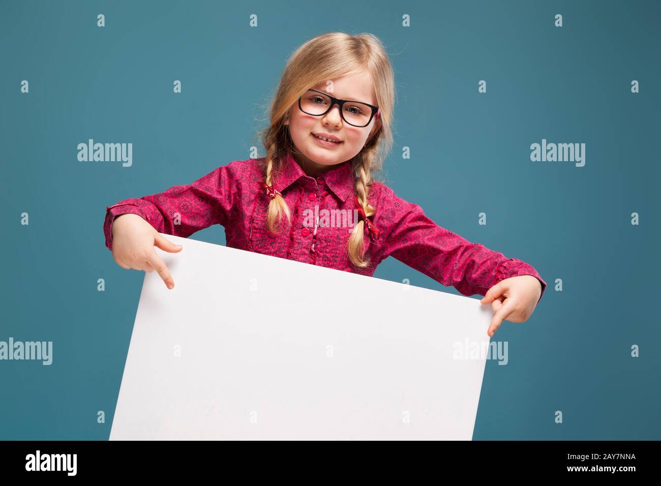 Adorable little girl in pink shirt, black trousers and glasses holds empty poster Stock Photo