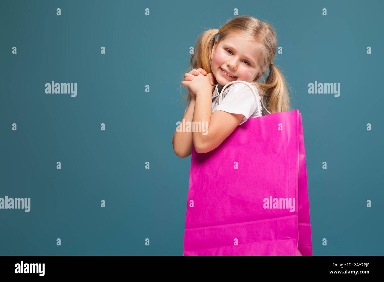 Adorable cute little girl in white shirt, white jacket and white shorts hold purple paper bag Stock Photo