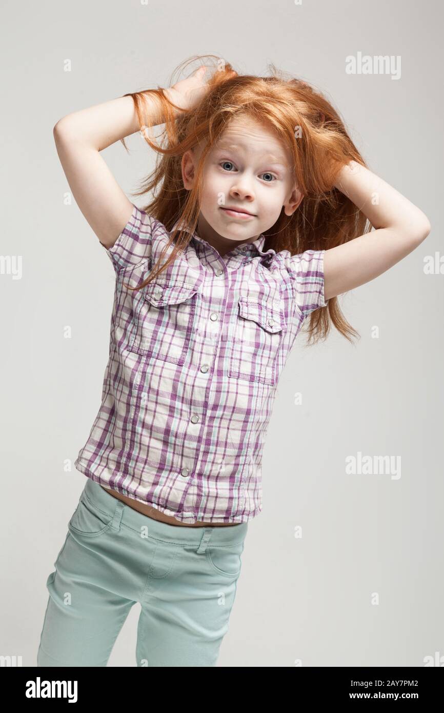 Beautiful redhead little girl in plaid shirt, bright blue trousers and