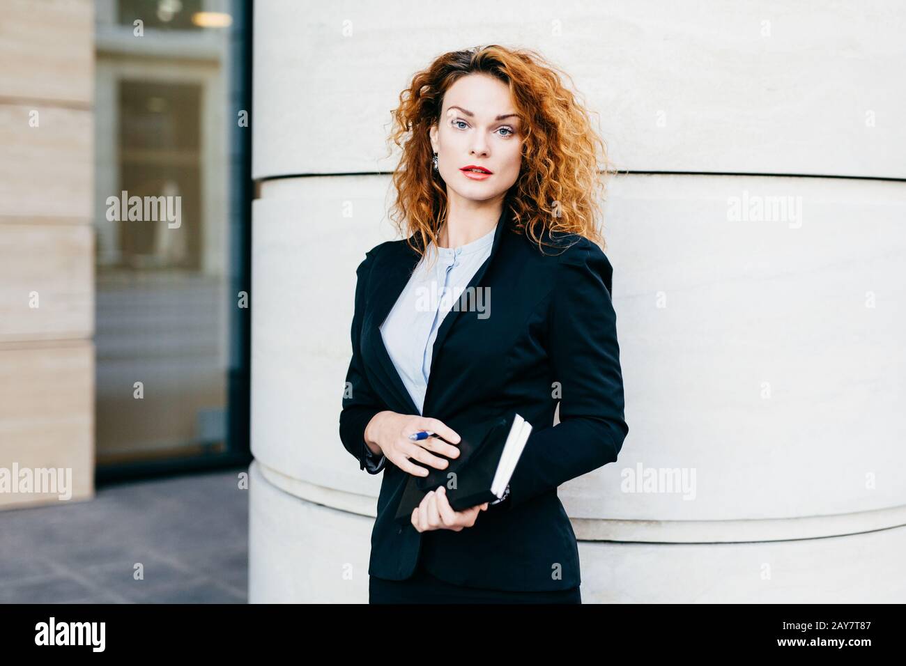 Young beautiful woman wearing formal clothes, dressed formally, holding pocketbook with pen, having bushy hairstyle, standing near office builduing. S Stock Photo - Alamy Young beautiful woman wearing formal clothes, dressed formally, holding pocketbook with pen, having bushy hairstyle, standing near office builduing. S Stock Photo - Alamy