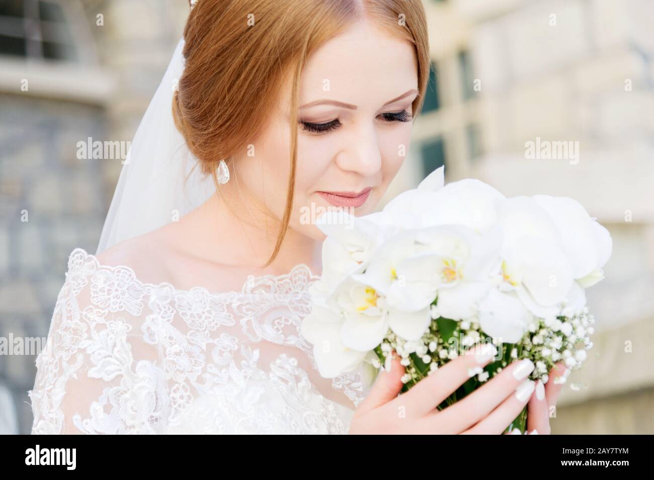 A young bride in a white dress is sniffing her wedding bouquet that is carefully held by her hands Stock Photo