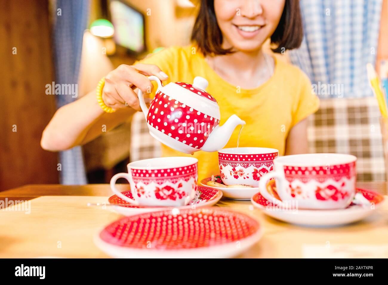 A girl in a cafe pours tea from a teapot into a mug. Stock Photo