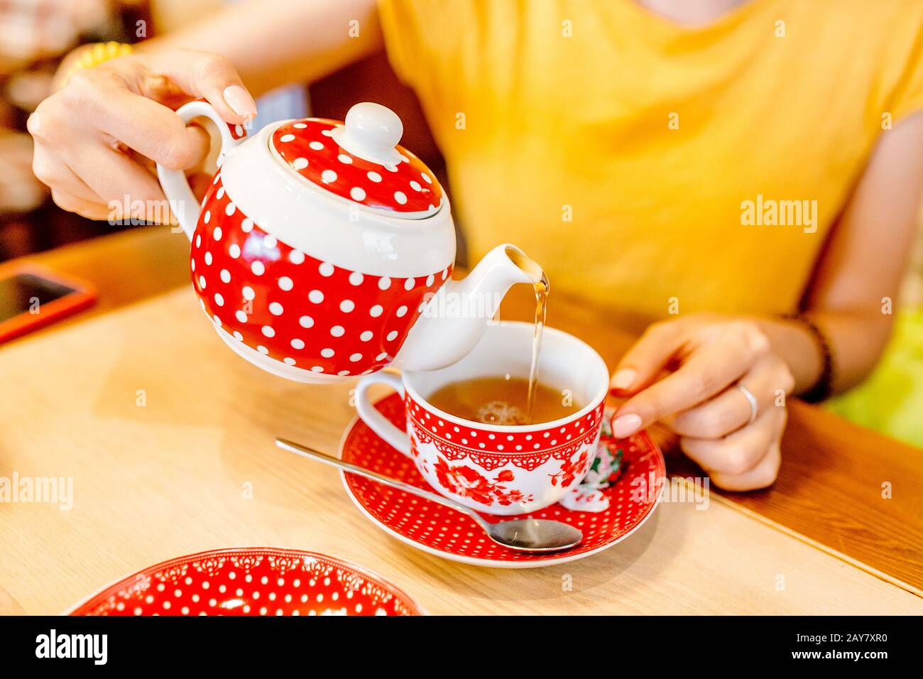 A girl in a cafe pours tea from a teapot into a mug. Stock Photo
