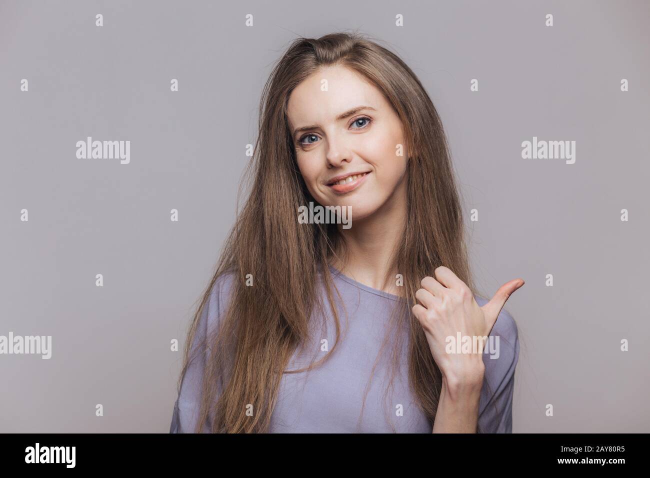 Isolated shot of pleased attractive brunette woman dressed casually, has happy expression, isolated over grey background with copy space for your adve Stock Photo