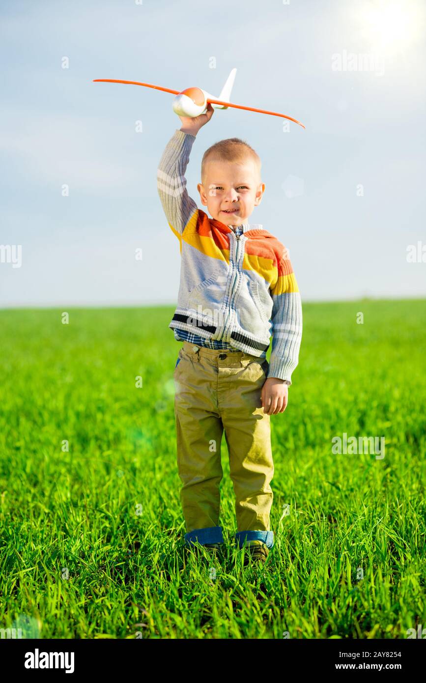 Happy boy playing with toy airplane against blue summer sky and green ...