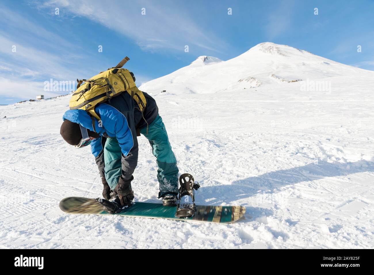 A snowboarder with a backpack on his back fastens snowboard bindings Stock Photo