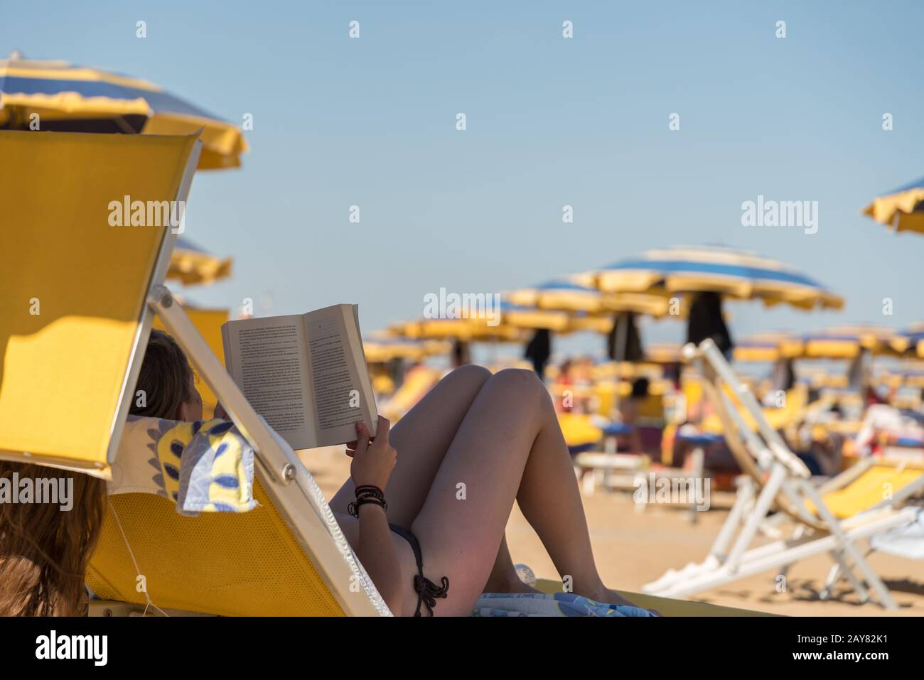 Summer holidaymaker reading a book on a sun lounger on a sandy beach Stock Photo