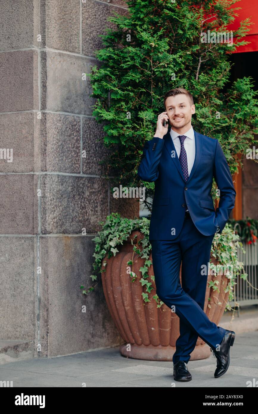 Clever handsome male manager in formal clothes, shares good news with business partner, being glad after successful meeting, wears formal clothes, sta Stock Photo
