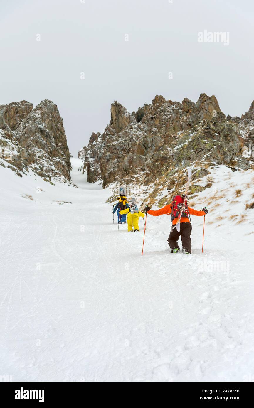 Extreme skiers climb to the top along the couloir between the rocks before the descent of the freeride backcountry Stock Photo