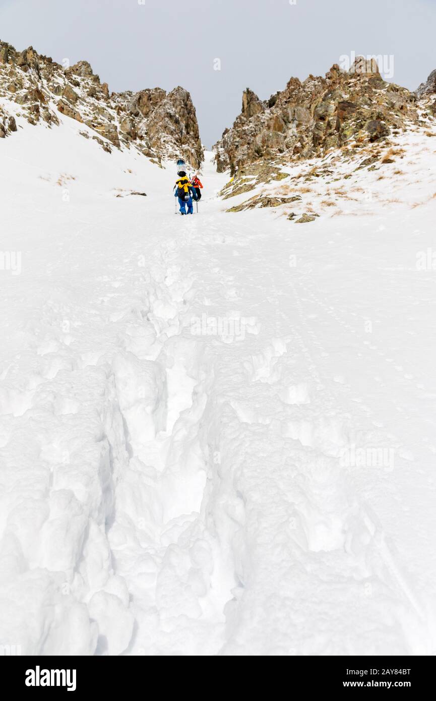 Extreme skiers climb to the top along the couloir between the rocks before the descent of the freeride backcountry Stock Photo