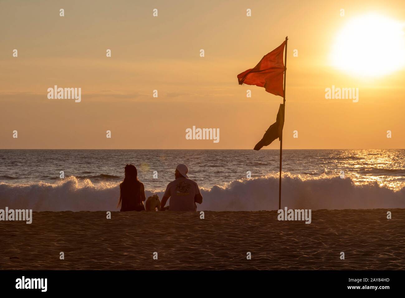 Brisas de Zicatela, Oaxaca, Mexico - A couple enjoys sunset on a Pacific Ocean beach. The red flag warns of dangerous swimming conditions. Stock Photo