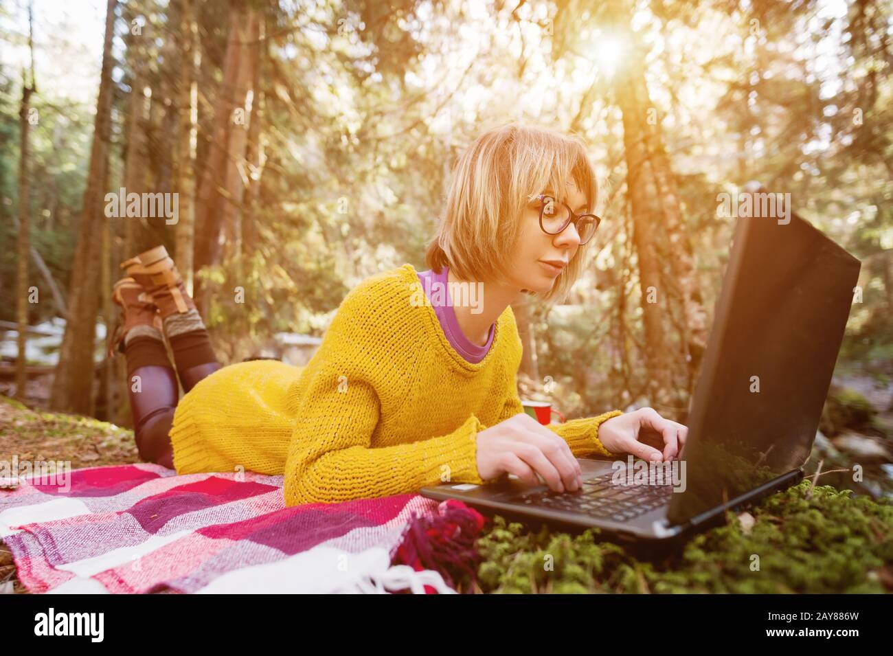 Toned image of a freelancer girl portrait in a yellow sweater and glasses looking thoughtfully at the laptop screen in the natur Stock Photo