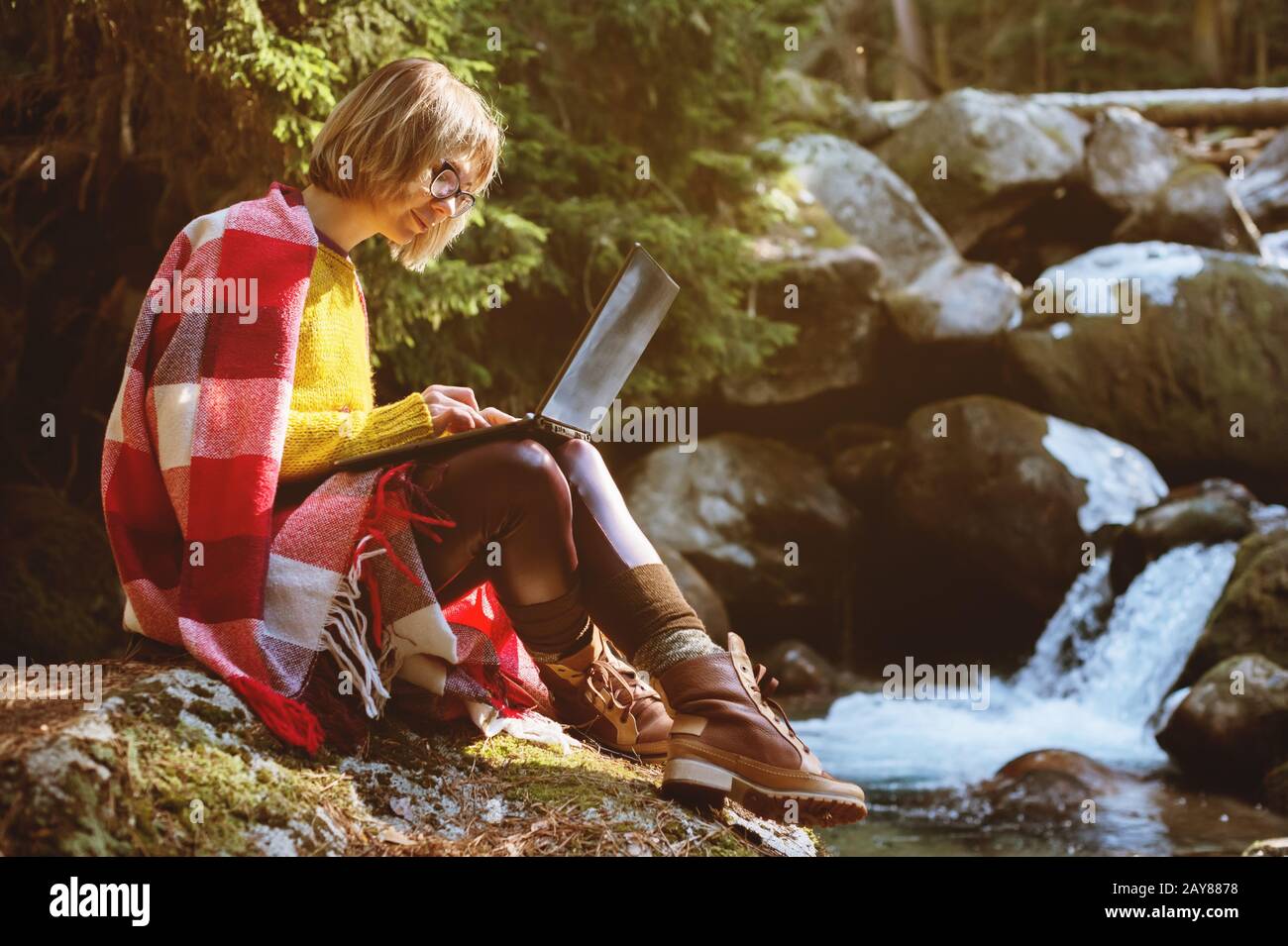 A toned portrait of a a smiling freelancer hipster girl with glasses dressed in a blanket with a laptop kneeling sitting on a ro Stock Photo