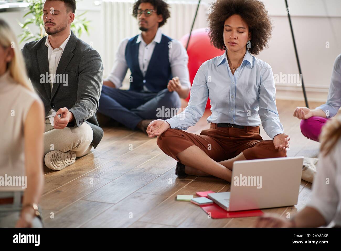 group of business coworkers meditating at work, sitting on the floor with legs crossed and eyes closed. modern, casual, business, meditation concept Stock Photo