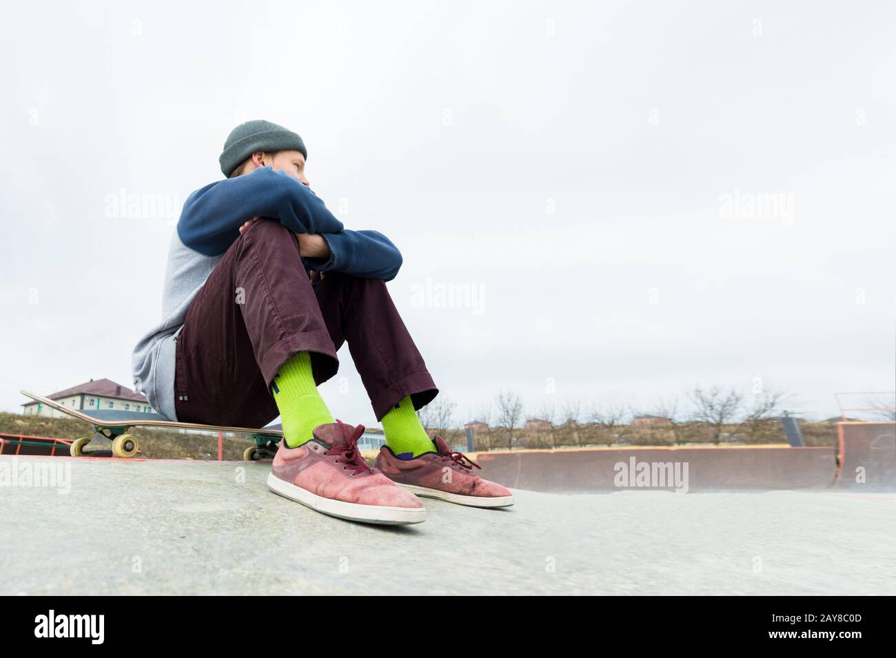 A teenage boy is sitting on a skateboard in the park. The concept of free time pastime for teenagers in the city Stock Photo