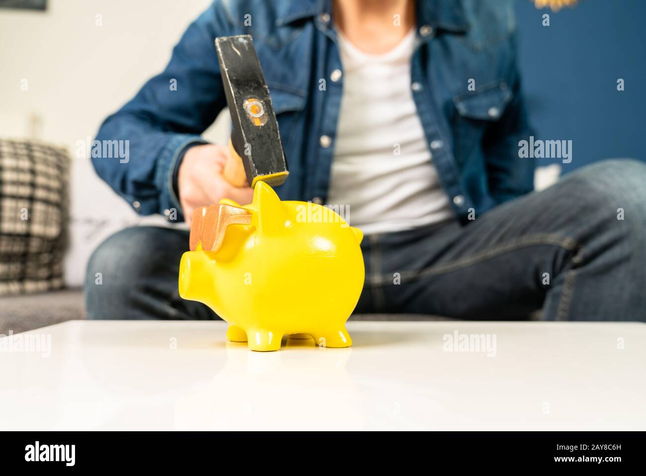 a man smashes his piggy bank on a table in his living room Stock Photo