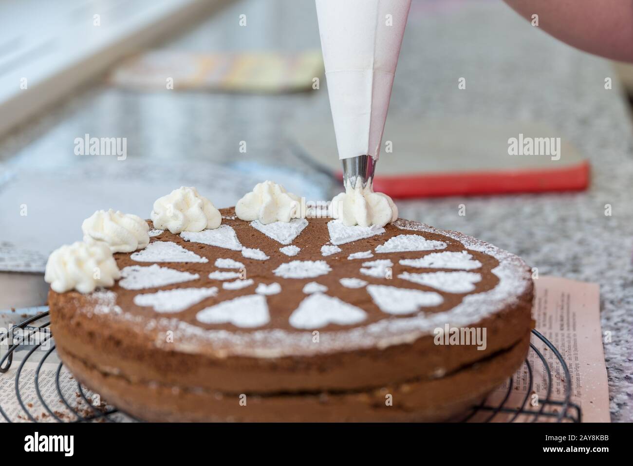 Confectioner decorates chocolate cake with sugar pattern and whipped cream - close-up Stock Photo
