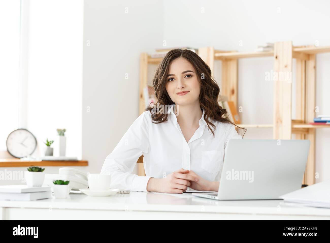 Portrait of smiling pretty young business woman sitting on workplace ...