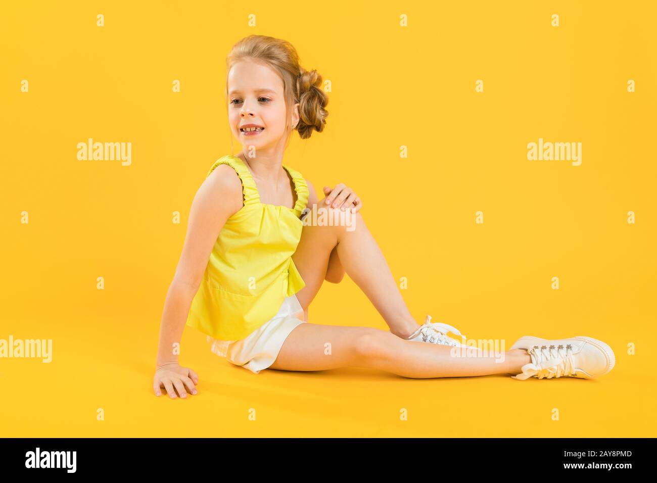 A teenage girl is sitting on a yellow background. Stock Photo