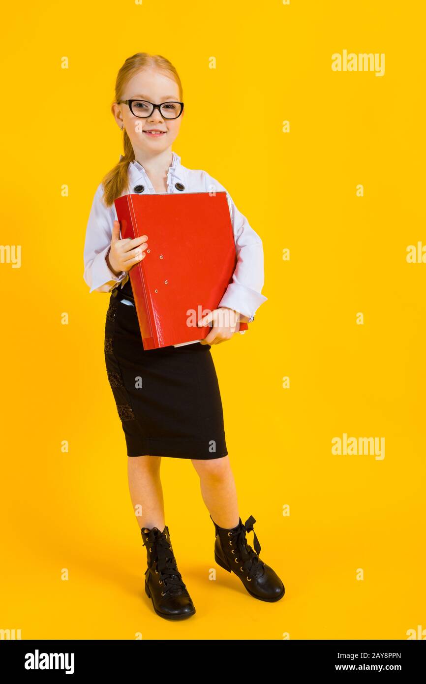 Girl with red hair on a yellow background. A charming girl in transparent glasses is holding a large red folder in her hands. Stock Photo