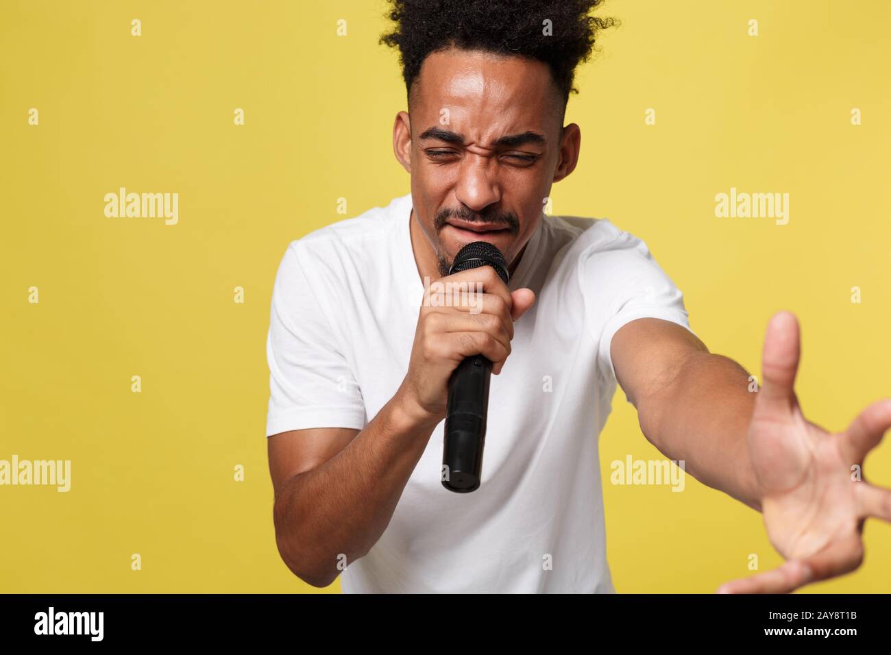 Stylish afro american man singing into microphone isolated on a yellow