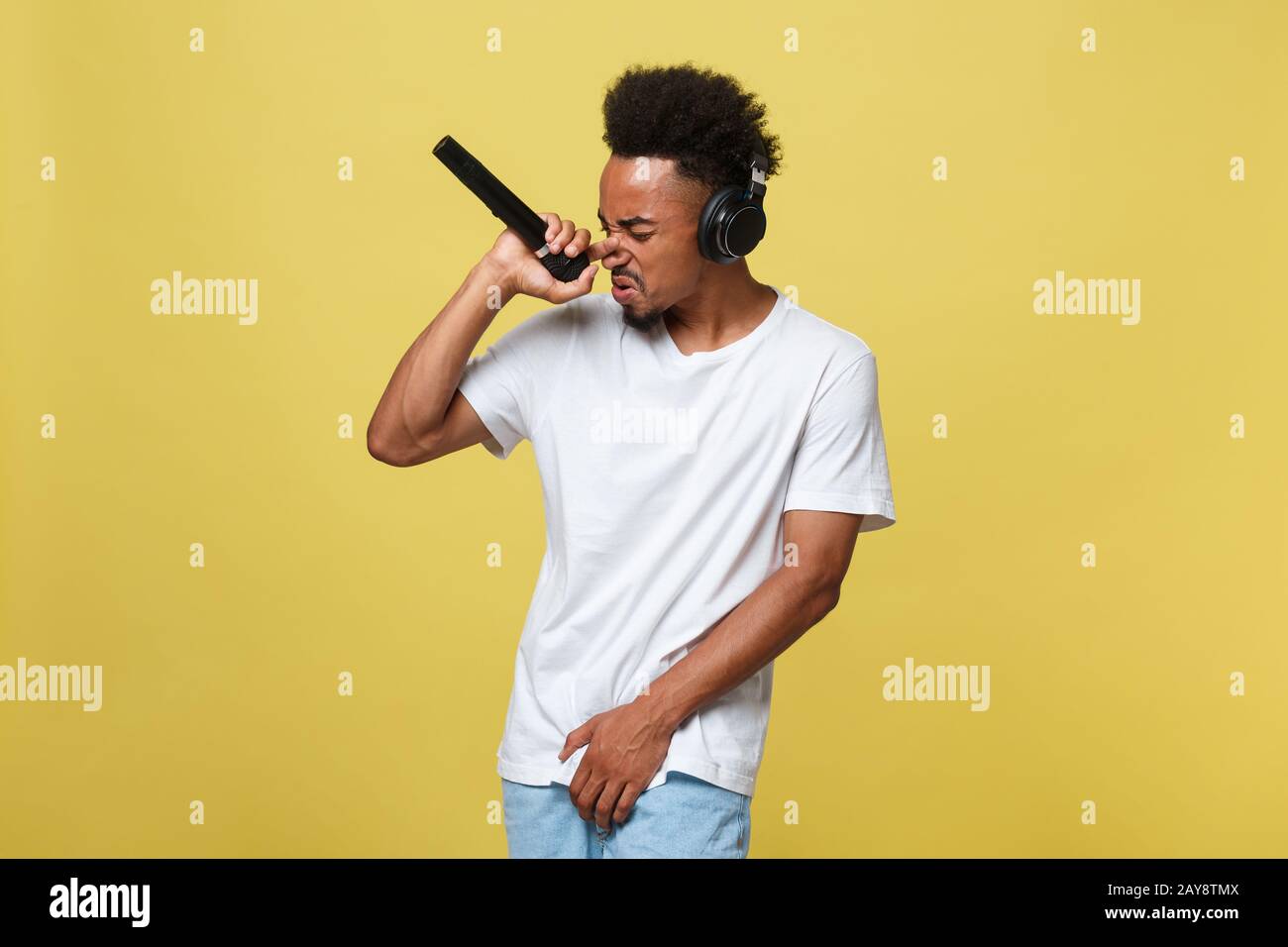 Attractive young dark-skinned man with afro haircut in white t shirt, gesticulating with hands and microphone, dancing and singi Stock Photo