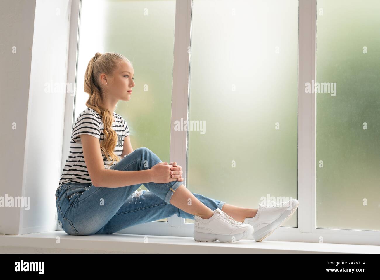 Pretty teenaged girl on window sill profile shot Stock Photo