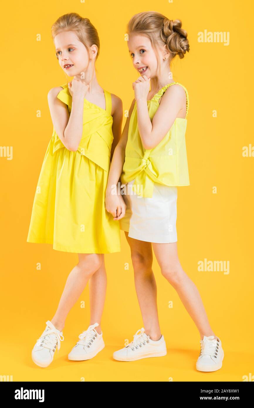 The girls of the twins stand together on a yellow background. Stock Photo