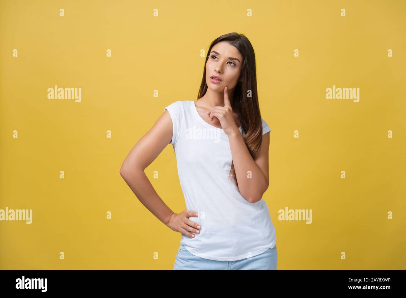 portrait of the beautiful young woman thinking on the yellow background ...