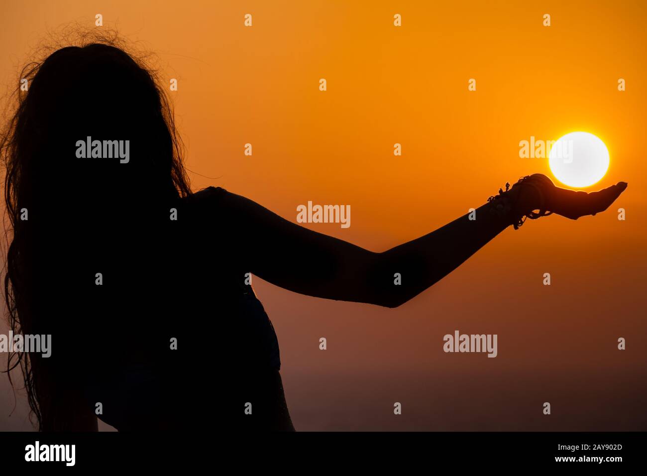 Girl silhouette, her palm appearing to be supporting the sun as it sets Stock Photo