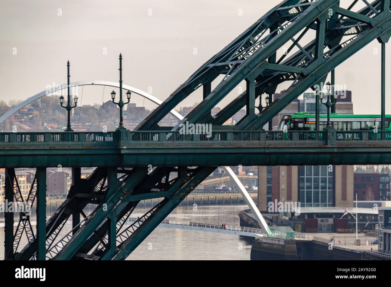 Green bus crossing the Tyne Bridge and Millennium Bridge in the distance at Newcastle Quayside on a cloudy day Stock Photo