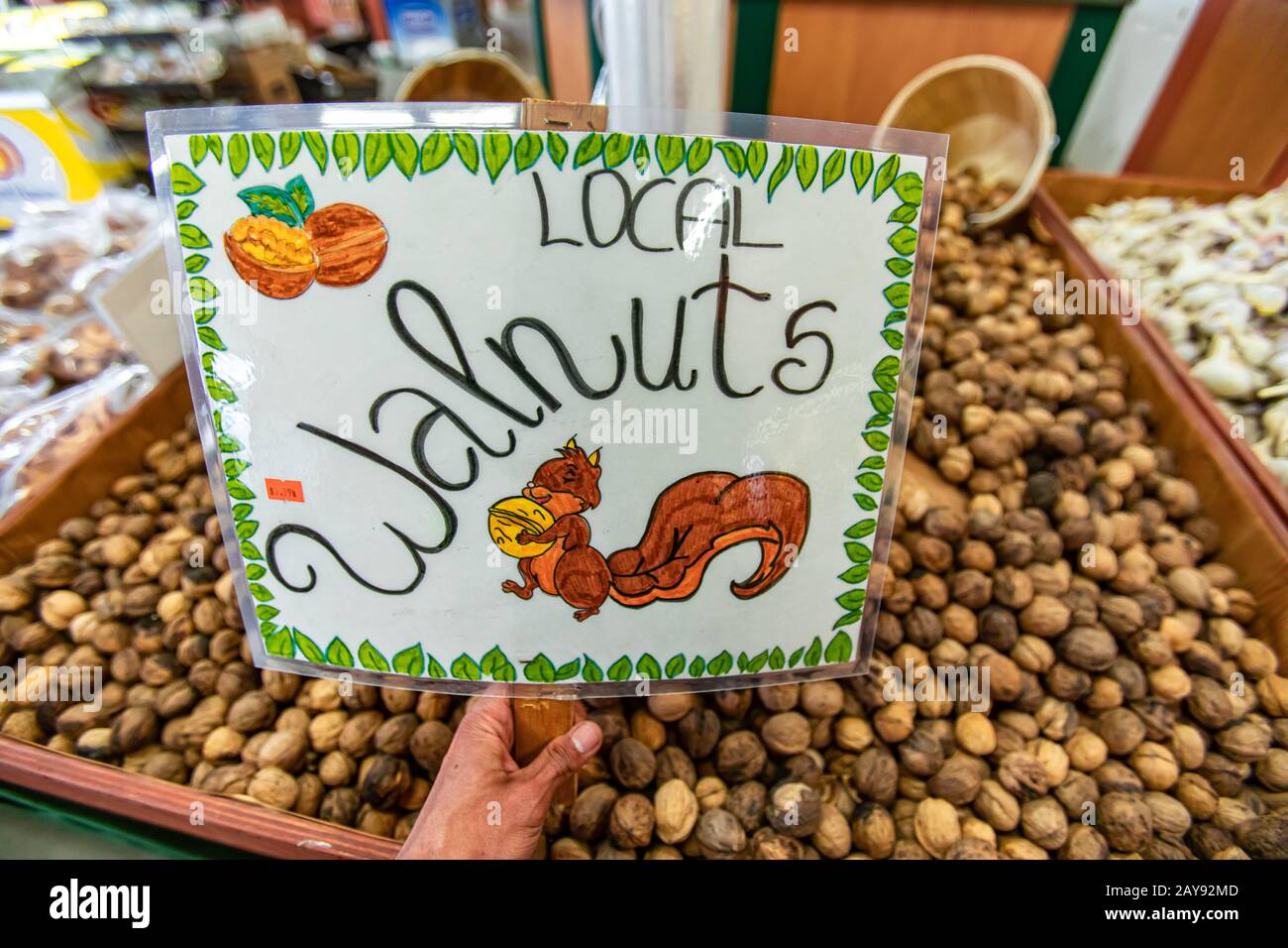 Dried walnuts on sale at the local food market. Hand written plasticized signboard. Drawing of happy and smiling squirrel holding a walnut. Stock Photo