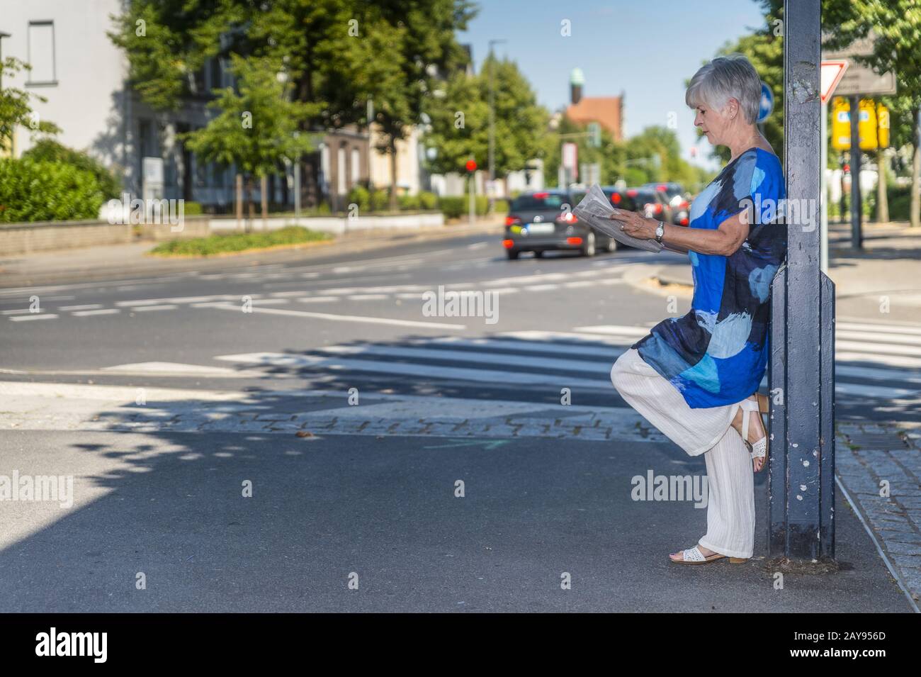 Senior citizen leans against a lamppost and reads newspaper. Stock Photo