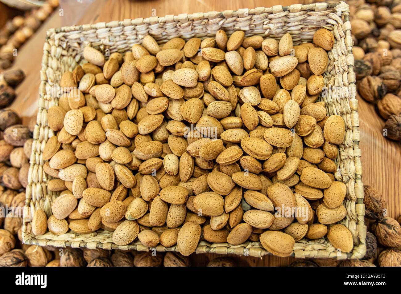 Close up of a basket of fresh, peeled almonds on sale at the local food market. Other dried fruits in the blurred background. Healthy snacks. Stock Photo