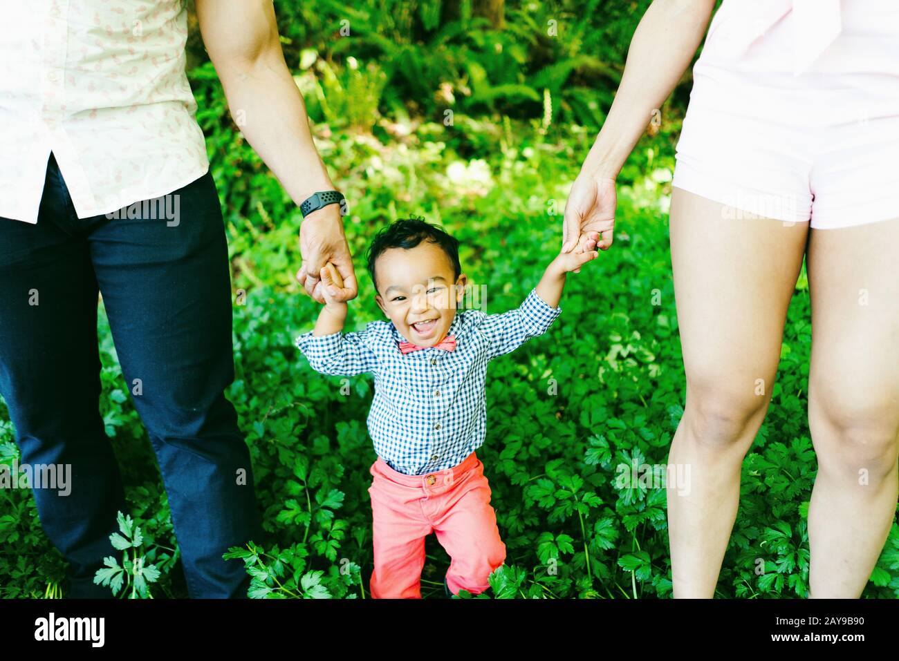 Cropped view of a smiling baby boy holding his parent's hands Stock Photo
