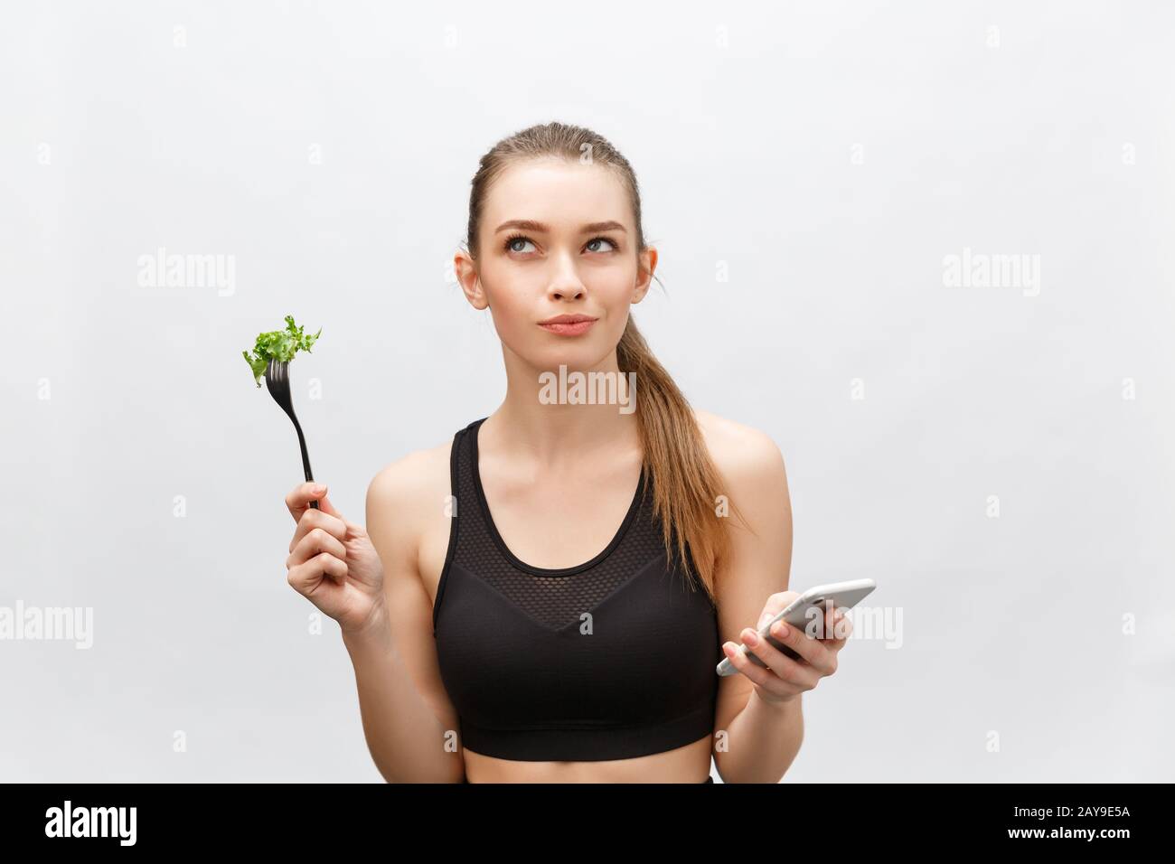 Beautiful young woman wearing sport clothes with salad in hand, using smart phone. Stock Photo